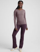 woman wearing a long-sleeve top and purple pants on a white background.